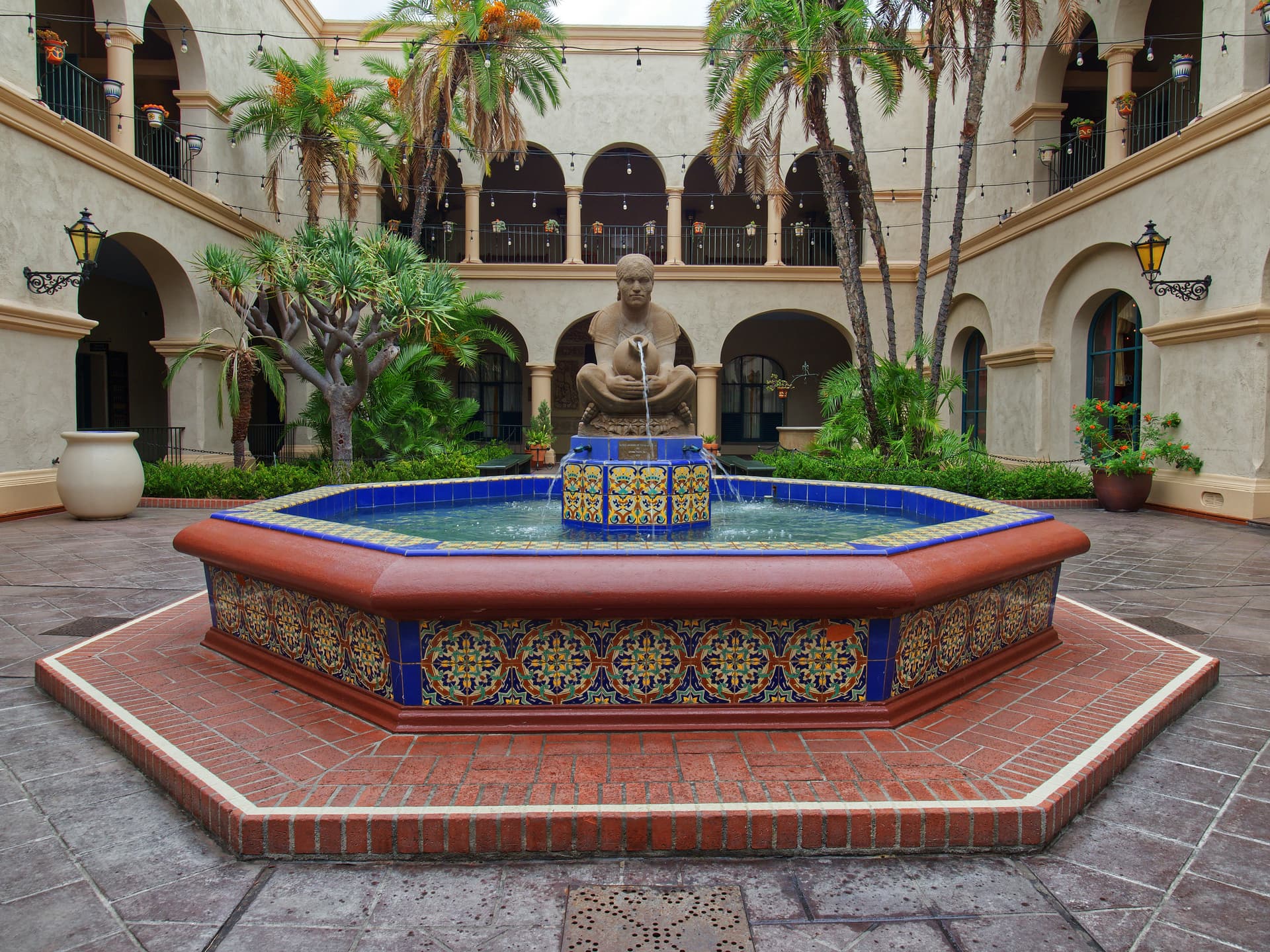 نافورةُ فناءٍ حجريّةٌ بماءٍ يسقطُ في حوضٍ ضحلٍ تحتَ ضوءِ عصرٍ ناعم